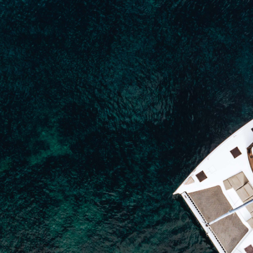 A drone view of a catamaran yacht anchored in a Mediterranean bay surrounded by dark emerald water