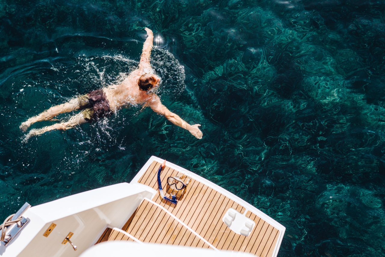 A man swimming in clear water by the swim platform on a yacht in the Mediterranean