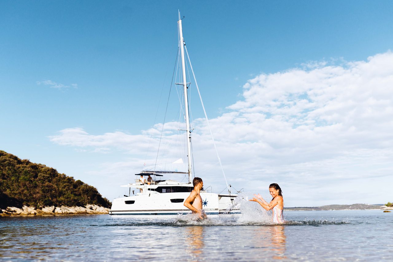 A man and a woman splashing water by their anchored sailing catamaran