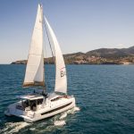 Bali 4.2 sailing near the coast with a man at the helm and women enjoying the foredeck and the flybridge