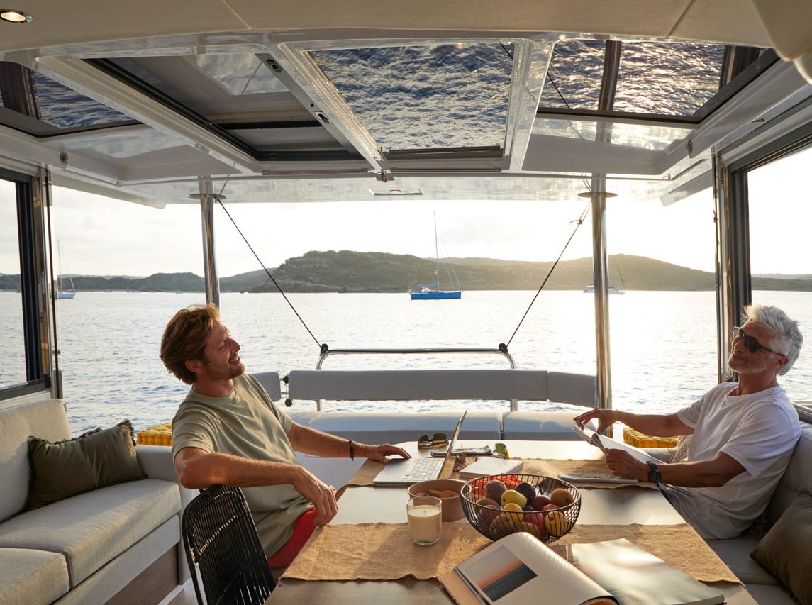 Men relaxing in the spacious and luminous cockpit of the Bali 4.4 sailing catamaran at sunset