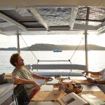 Men relaxing in the spacious and luminous cockpit of the Bali 4.4 sailing catamaran at sunset