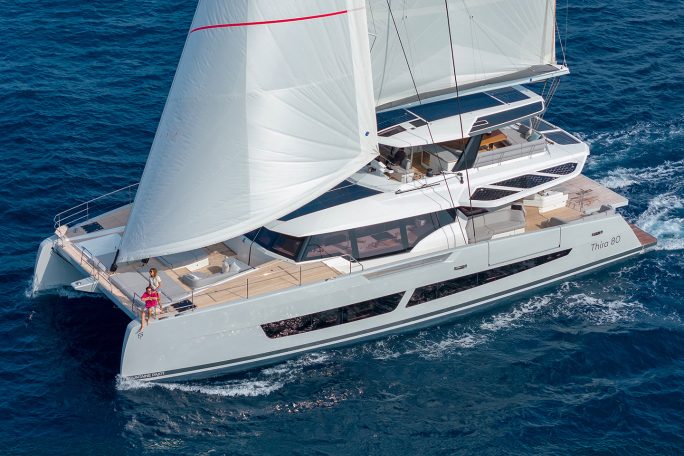 Rear view of the Fountaine Pajot Thira 80 sailing with a couple on the foredeck