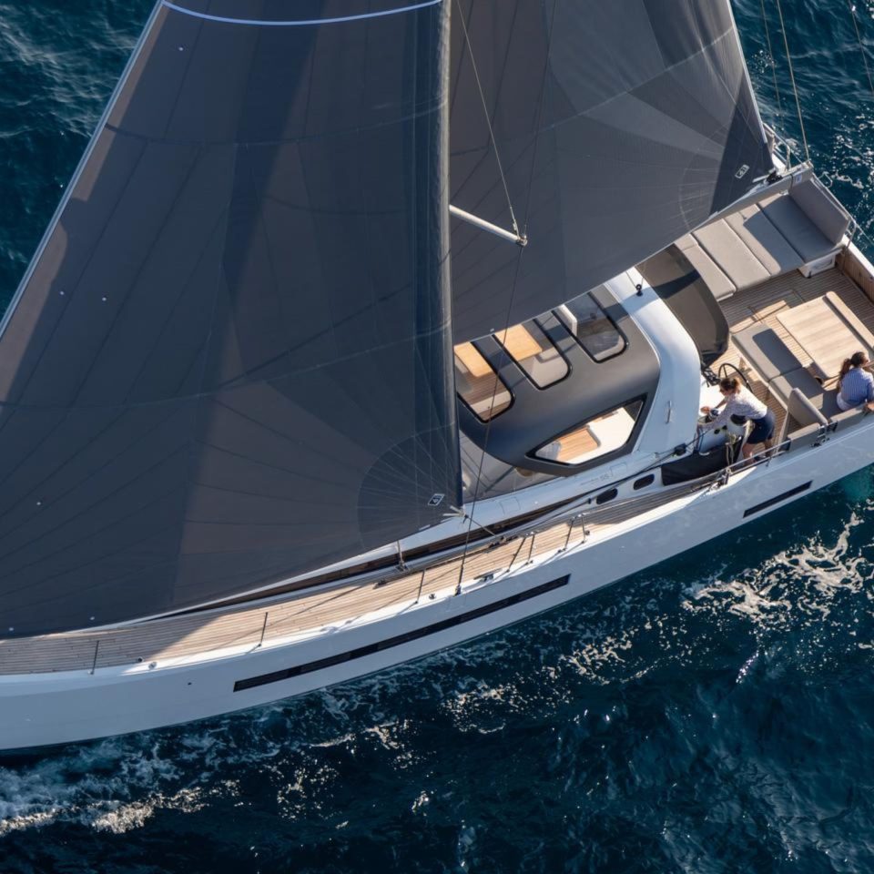 Aerial top view of the Jeanneau 55 sailing in deep blue water with a woman at the helm and a couple enjoying the cockpit