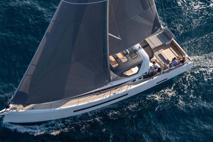 Aerial top view of the Jeanneau 55 sailing in deep blue water with a woman at the helm and a couple enjoying the cockpit