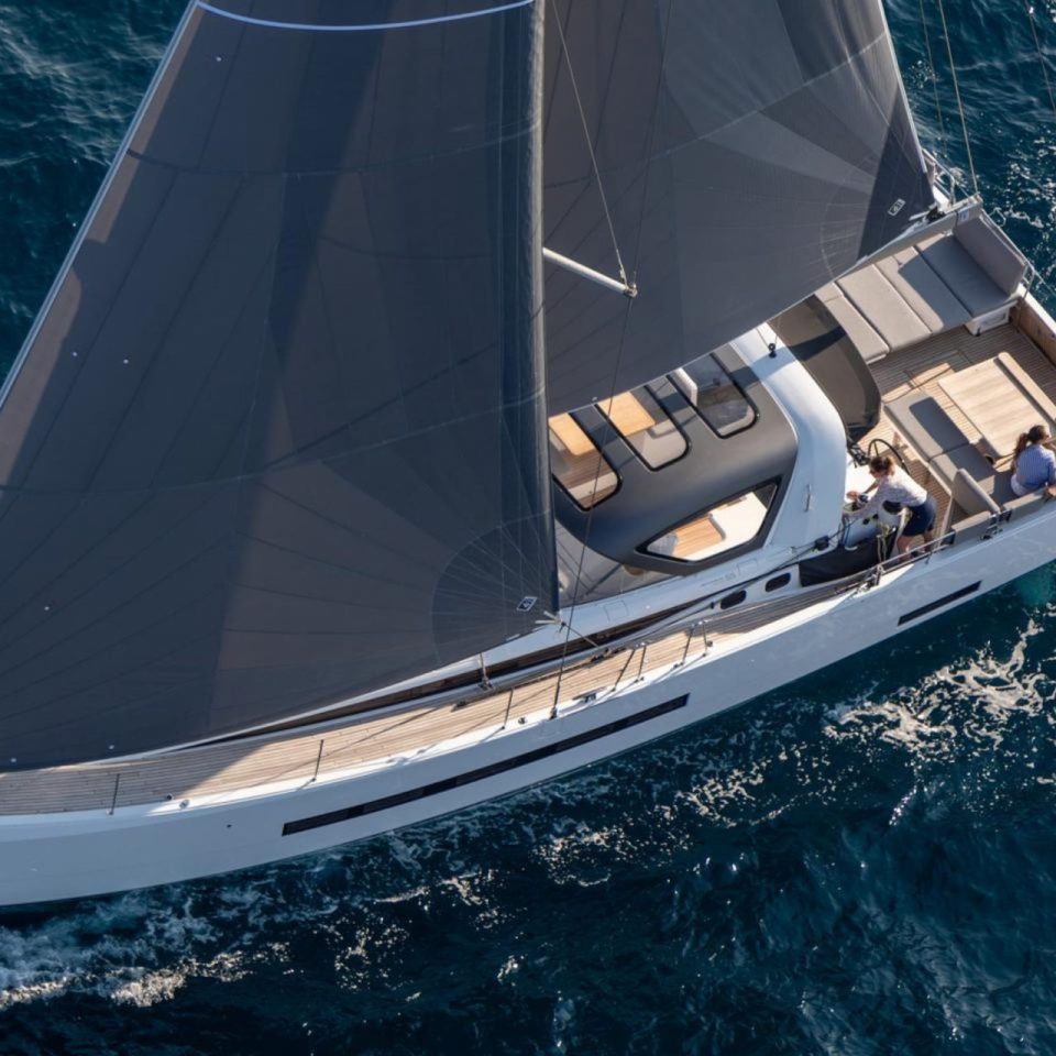 Aerial top view of the Jeanneau 55 sailing in deep blue water with a woman at the helm and a couple enjoying the cockpit