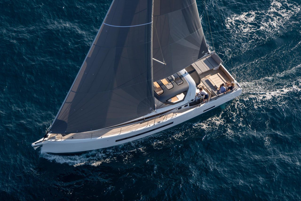 Aerial top view of the Jeanneau 55 sailing in deep blue water with a woman at the helm and a couple enjoying the cockpit