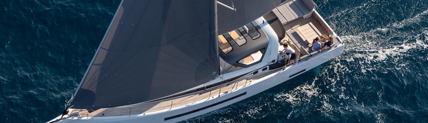 Aerial top view of the Jeanneau 55 sailing in deep blue water with a woman at the helm and a couple enjoying the cockpit