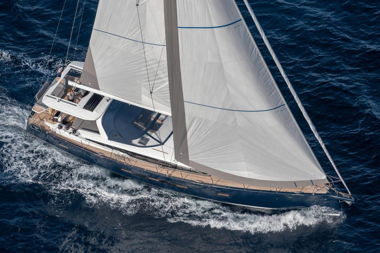 Aerial top view of the Jeanneau Yacht 65 sailing in deep blue water with a woman in the cockpit and a man at the helm