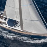 Aerial top view of the Jeanneau Yacht 65 sailing in deep blue water with a woman in the cockpit and a man at the helm