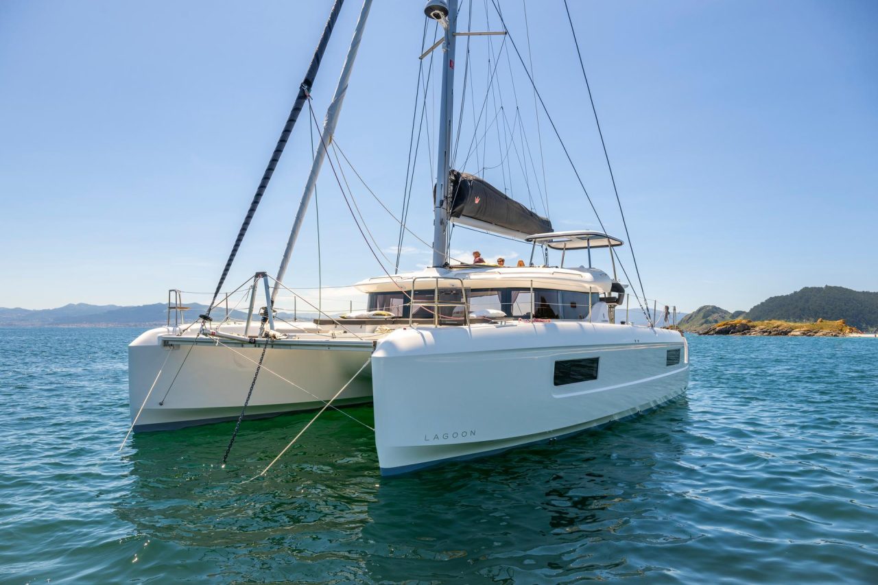 Front view of the Lagoon 43 sailing catamaran at anchor with guests enjoying the flybridge