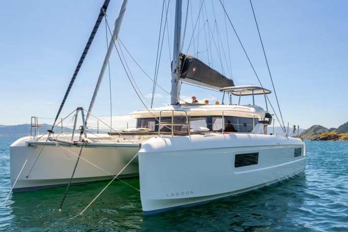 Front view of the Lagoon 43 sailing catamaran at anchor with guests enjoying the flybridge