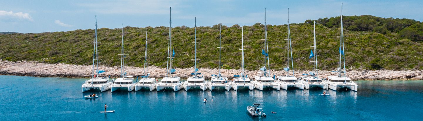 Many sailing catamarans lined up side by side in a Mediterranean bay