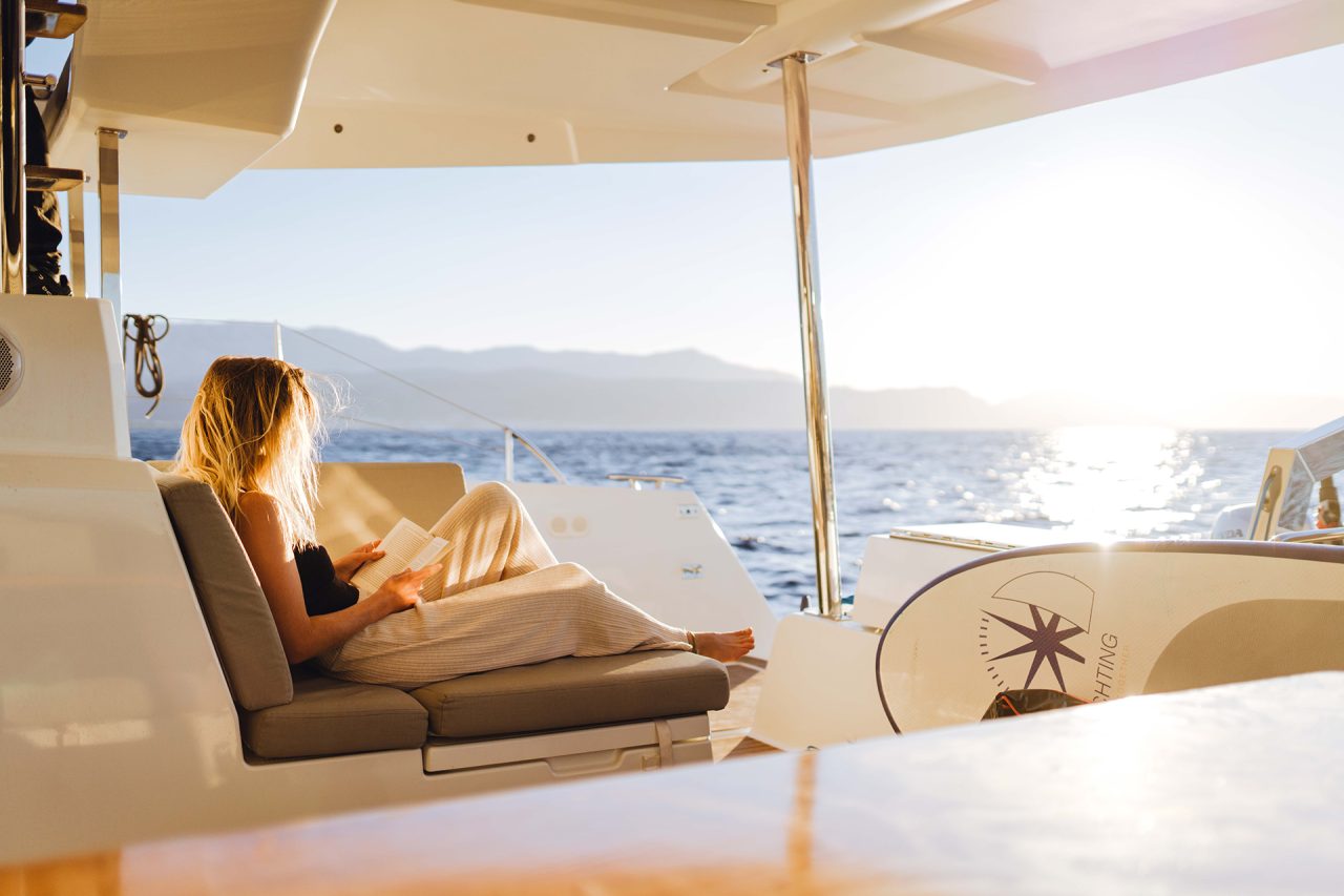 A woman reading in the aft cockpit onboard a sailing catamaran