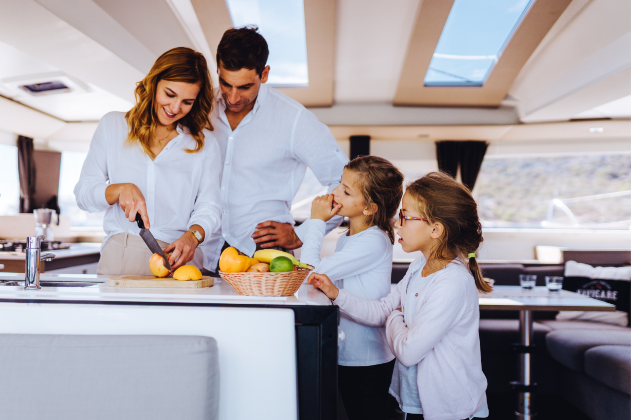 A family cutting up fruit in the galley of a sailing catamaran interior