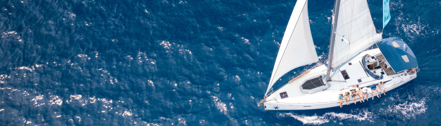 People sitting on the deck of the side hull on a sailing yacht while underway, surrounded by blue water