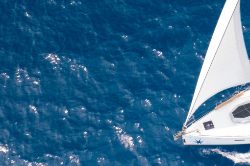 People sitting on the deck of the side hull on a sailing yacht while underway, surrounded by blue water