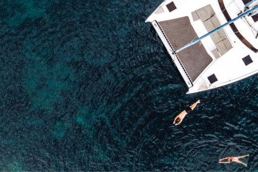 Drone image of people swimming in the clear water beside a sailing catamaran