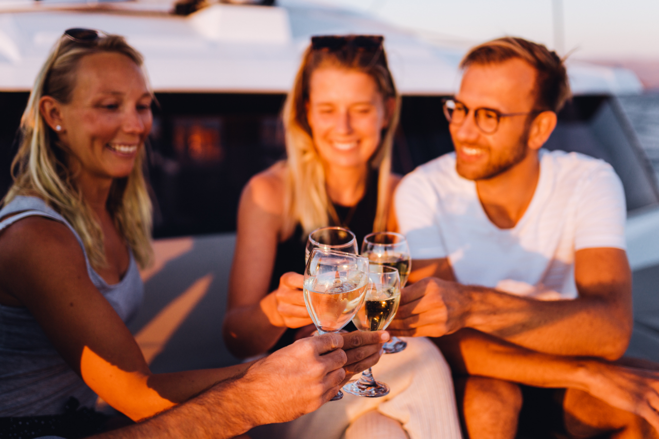 A group of people toasting and smiling at sunset on board a catamaran yacht