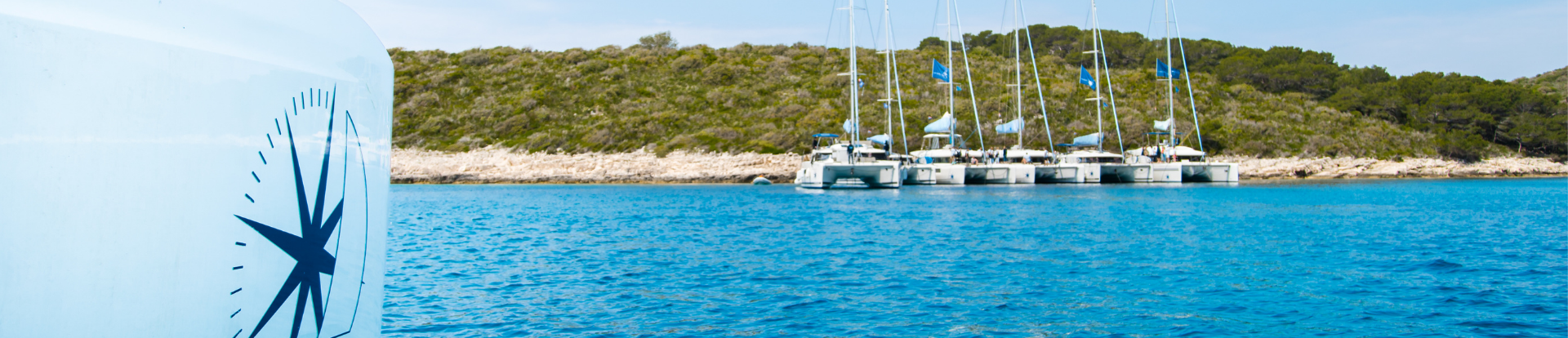 A close-up of a side hull with a Navigare logo and anchored sailing catamarans side by side in the distance