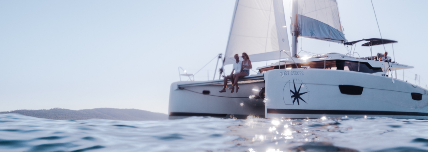A man and a woman sitting on the foredeck of a sailing catamaran while underway