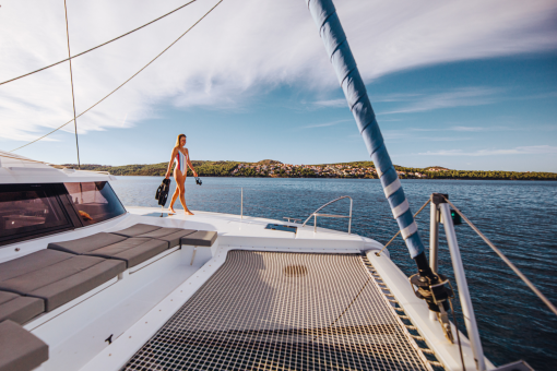 A woman walking on the foredeck of a sailing catamaran by the trampoline and forward sunbeds