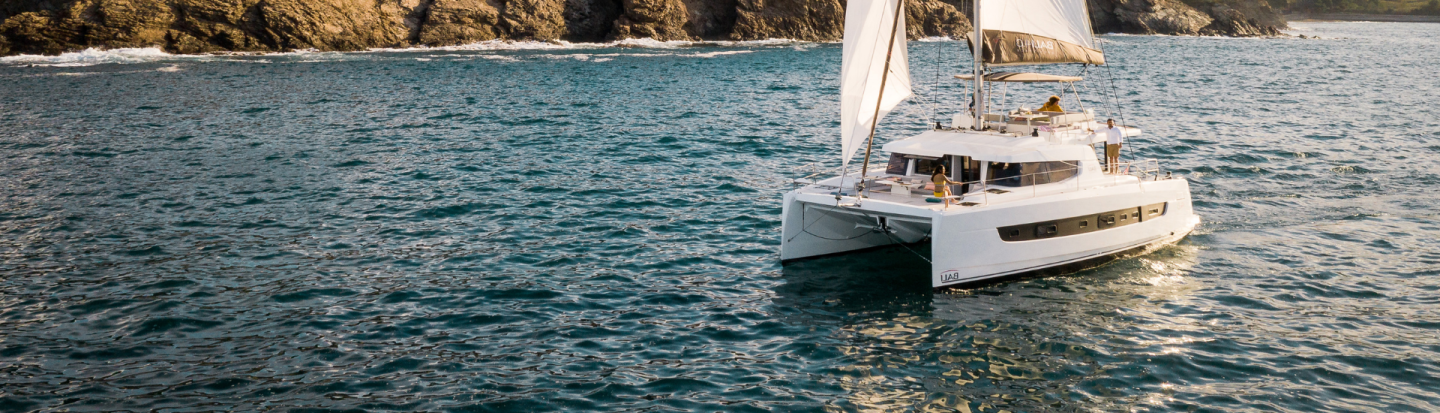 A bali sailing catamaran sailing with a rugged coastline in the background