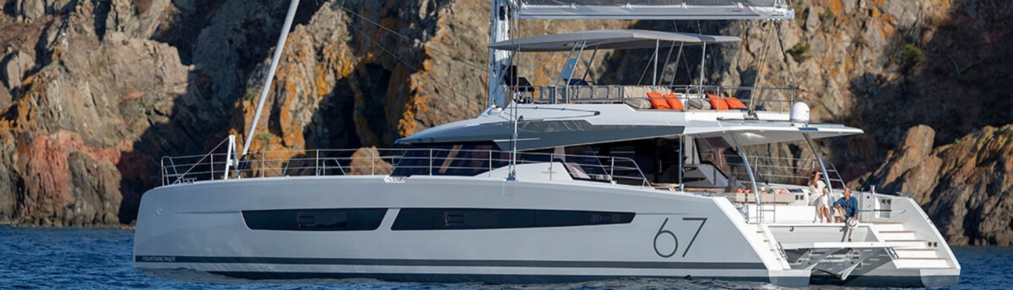A Fountaine Pajot 67 catamaran at anchor with dramatic cliffs in the background