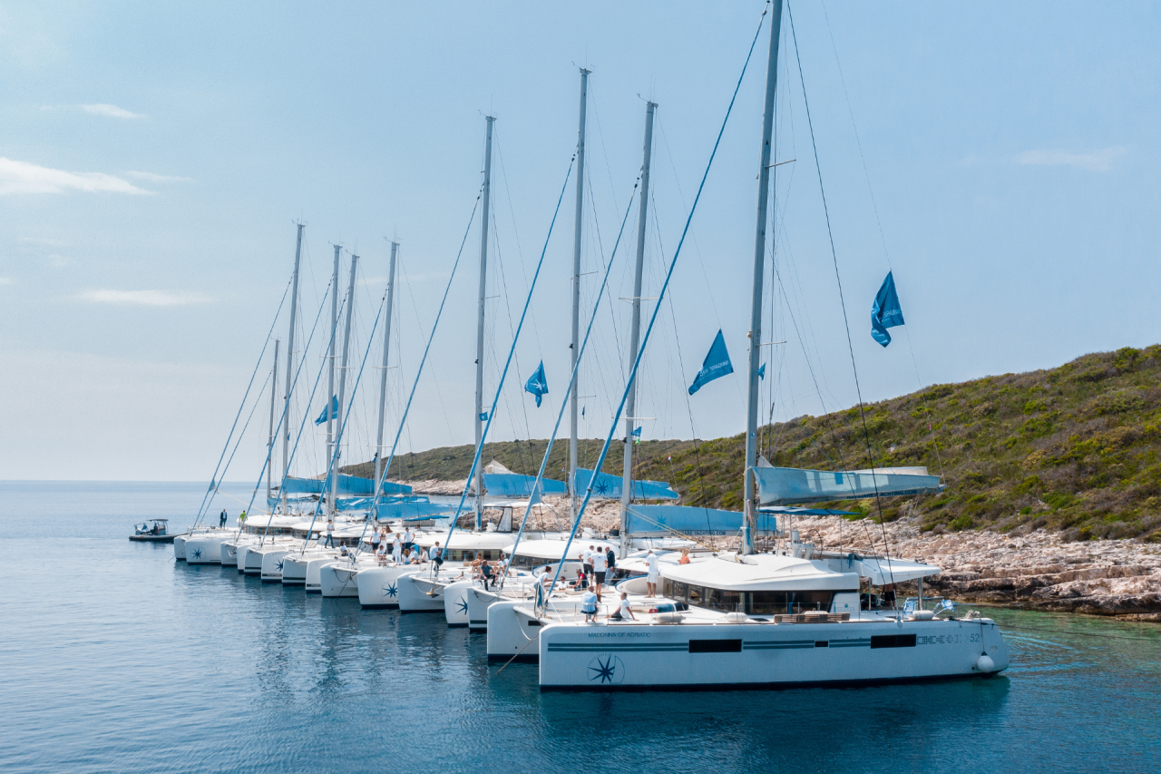 Many sailing catamarans lined up and anchored side by side in a Mediterranean bay