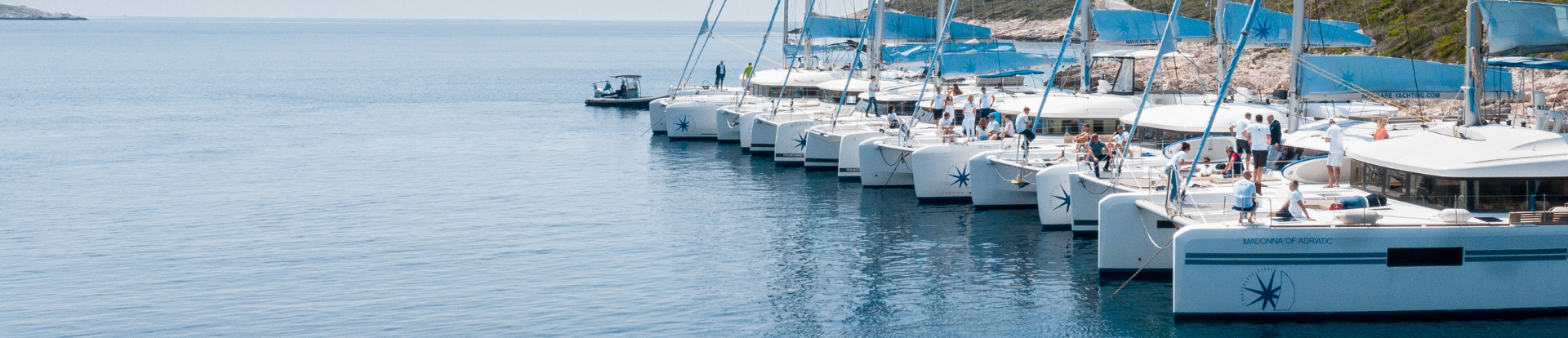 Sailing catamarans lined up side by side at anchor with people on board in the Mediterranean