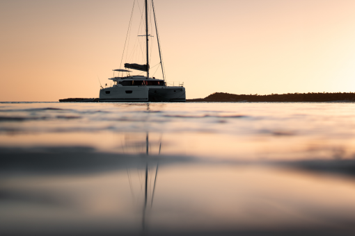 A sailing catamaran anchored at sunset