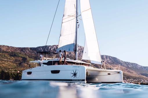 A couple walking holding hands on the deck of a sailing catamaran while underway