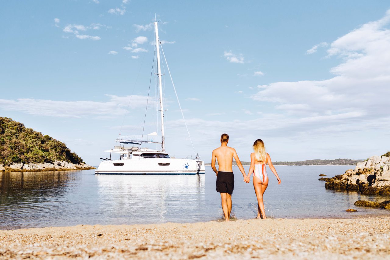 Couple on the beach looking at their catamaran at anchor - Owner experience