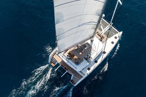 A catamaran yacht with sails up underway, seen from above.