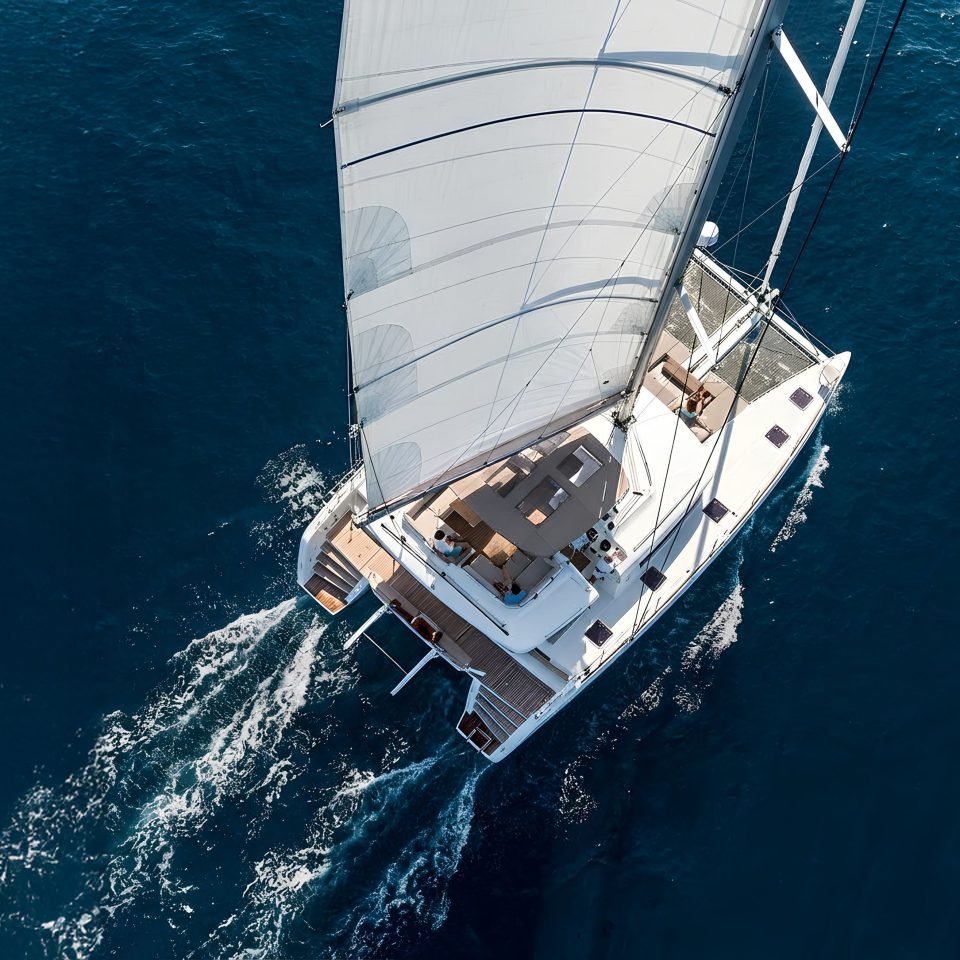 A catamaran yacht with sails up underway, seen from above.