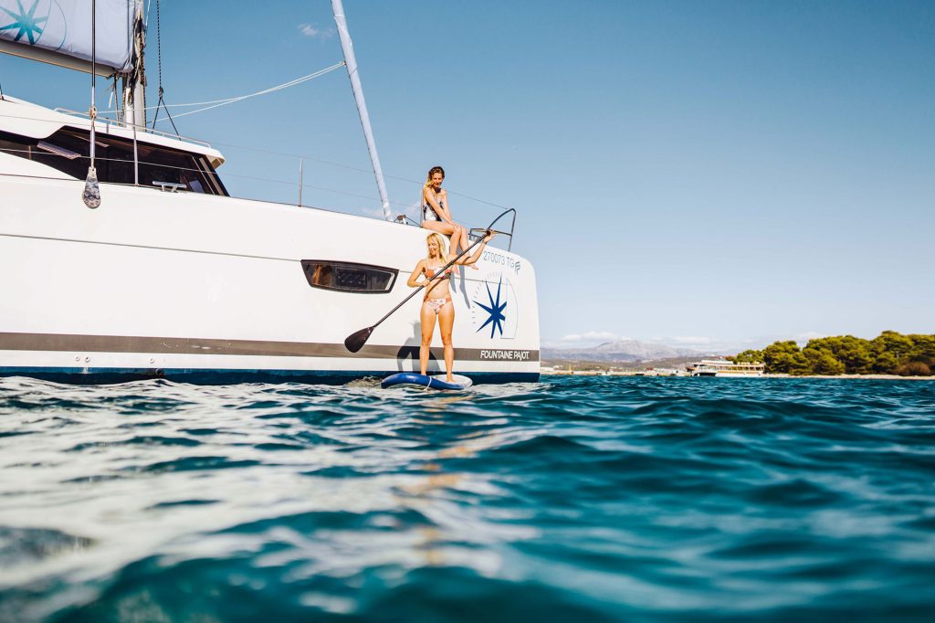 A woman on a paddleboard beside the hull at anchor.