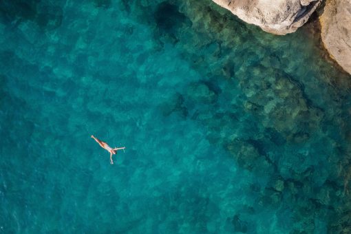 Aerial photo of a person happily floating in crystal blue sea water in Greece