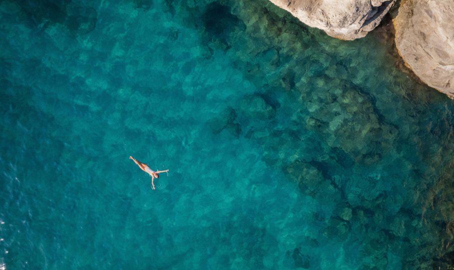 Aerial photo of a person happily floating in crystal blue sea water in Greece